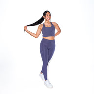 Woman in FLOWERS sports bra GUGA showing three-quarter angle, highlighting the feminine floral pattern in purple tones and flattering neckline cut